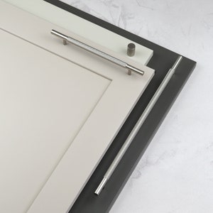 May include: Two cabinet door pulls, one silver and one black, with a textured, ridged design. The pulls are mounted on white and gray cabinet doors.