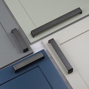 May include: Close-up of several cabinet door samples in various colors, each with a dark gray, rectangular handle. The doors are painted in shades of gray, blue, and white, showcasing the hardware's design and finish.