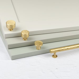 May include: Four gold-toned cabinet knobs and a matching pull with a hammered finish. The knobs are round and the pull is rectangular.