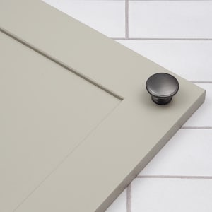 May include: A black cabinet knob with a round, slightly domed shape. The knob is mounted on a light gray cabinet door.