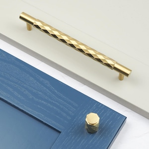 May include: A gold-toned cabinet pull with a diamond-shaped pattern and a matching knob. The pull is 12 inches long and the knob is 1 inch in diameter.