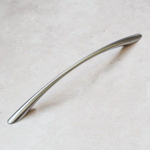 Peut inclure: Une poignée de cabinet incurvée de couleur argentée avec une finition lisse et arrondie.