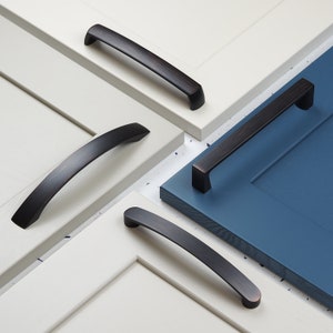 Può includere: Quattro maniglie per armadietti nere con finitura spazzolata. Le maniglie sono mostrate su ante di armadietti bianche e blu.