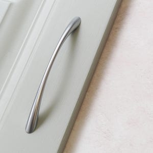 May include: A silver cabinet door handle with a curved design.