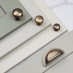 Può includere: Quattro pomelli per armadi e una maniglia per armadi in finitura ottone anticato. I pomelli sono rotondi e la maniglia ha una forma semicircolare.