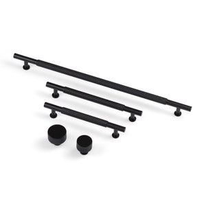 Könnte beinhalten: Satz mit vier schwarzen Metall-Schrankgriffen mit strukturierter Oberfläche. Die Griffe sind in verschiedenen Größen, wobei der größte etwa 30 cm lang ist. Zwei kleinere schwarze Metallknöpfe sind ebenfalls enthalten.