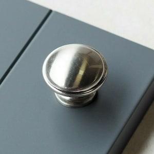 Può includere: Un pomello rotondo per armadio in argento con un bordo rialzato.