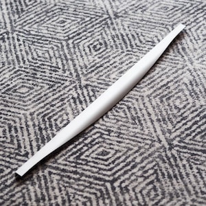 Könnte beinhalten: Ein langer, dünner, weißer Metallgriff mit einer leichten Biegung. Der Griff liegt auf einem gemusterten Teppich.