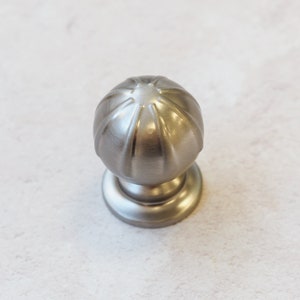 May include: A silver knob with a round, fluted design. The knob has a smooth, polished finish.