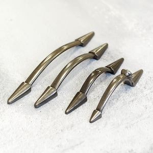 May include: Four silver-toned metal cabinet pulls with pointed ends. The pulls are arranged in a row from largest to smallest.