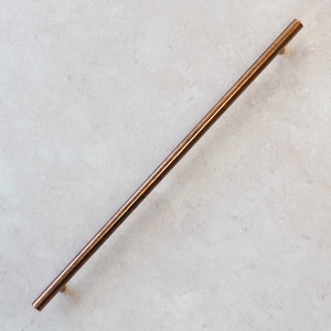 Op de afbeelding: Een lange, dunne, koperkleurige metalen staafgreep. De greep is glad en heeft afgeronde uiteinden.