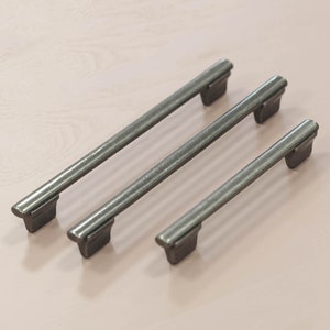 May include: Three silver metal cabinet pulls of varying lengths. The pulls are rectangular with rounded ends.