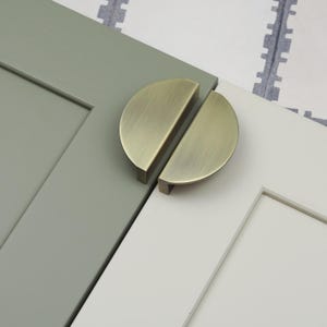 Peut inclure: Deux poignées de porte de placard en demi-cercle en laiton brossé. Les poignées sont montées sur une porte de placard verte et blanche.