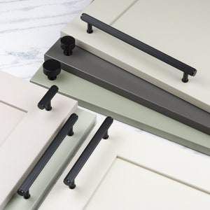 Könnte beinhalten: Schwarze Schrankbeschläge, einschließlich Knöpfe und Griffe, die auf verschiedenen farbigen Schranktüren gezeigt werden. Die Beschläge haben ein modernes, minimalistisches Design.