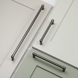 May include: Three different sizes of black metal cabinet pulls with rounded ends. The pulls are shown mounted on white and green cabinet doors.