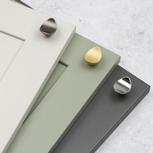 以下が含まれることがあります： 白、緑、グレーの3つのキャビネットドアに、異なる色のキャビネットノブが付いています。ノブは涙の形をしていて、金属製です。ノブはシルバー、ゴールド、ブラックです。