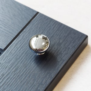 Pode incluir: Um botão redondo de armário cromado com uma superfície brilhante e reflexiva.