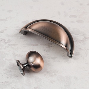 May include: Two antique copper cabinet hardware pulls. One is a cup pull and the other is a round knob.