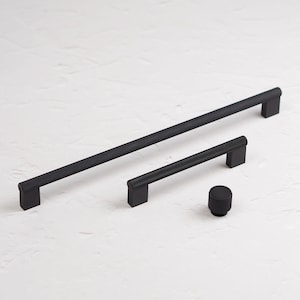 May include: Three black metal cabinet pulls with a textured finish. The pulls are in different sizes. The largest pull is 12 inches long, the medium pull is 6 inches long, and the smallest pull is 1 inch in diameter.