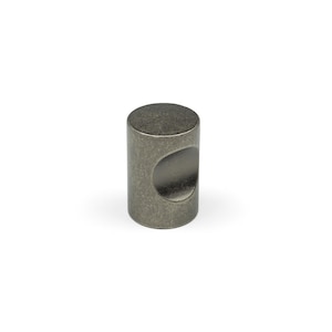 Puede incluir: Un pomo cilíndrico para muebles con un acabado metálico oscuro y desgastado. El pomo presenta una parte superior plana y lisa y una hendidura cóncava distintiva en un lado para facilitar el agarre. La superficie tiene una textura gris moteada.