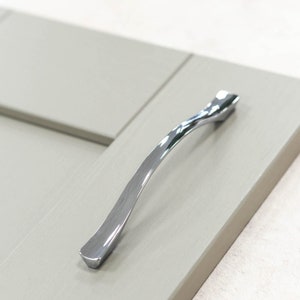 Pode incluir: Uma maçaneta de porta de armário de prata com um design curvo.