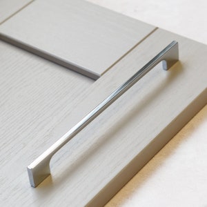 May include: A silver cabinet door handle with a rectangular shape and a slightly curved design.