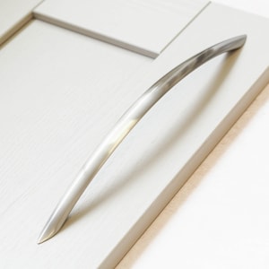 Könnte beinhalten: Ein gebogener Kabinetttürgriff aus gebürstetem Nickel.