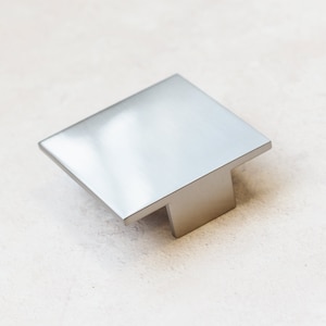May include: A silver square cabinet pull with a T-shaped base.