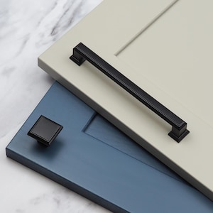 May include: Two cabinet doors with black cabinet hardware. The top door is a light gray color and features a long, rectangular pull handle. The bottom door is a dark blue color and features a small, square knob.
