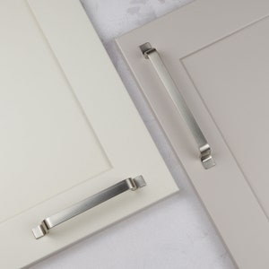 Può includere: Due ante di armadio con finiture diverse, una bianca e una grigio chiaro, ciascuna con una maniglia per armadio in nichel spazzolato.