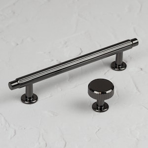 May include: Black cabinet hardware set with a long, ridged bar handle and a round knob with a ridged edge.