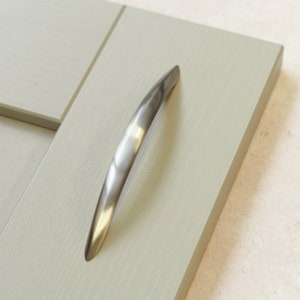 Puede incluir: Una manija de puerta de armario de plata con un diseño curvo.