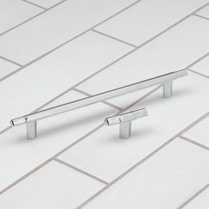 May include: Two chrome cabinet pulls, one long and one short, with a geometric design. The pulls are on a white tiled surface.