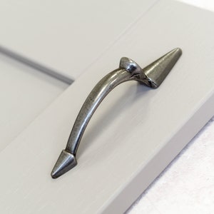 Może przedstawiać: Srebrny uchwyt do drzwi szafki o zakrzywionym kształcie i spiczastych końcach.