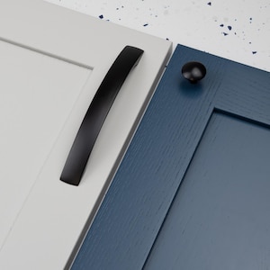 Può includere: Ferramenta nera per mobili, tra cui una maniglia curva e un pomello rotondo, esposta su ante di armadi bianche e blu. La maniglia è lunga circa 15 cm. Il pomello è un design semplice e rotondo.
