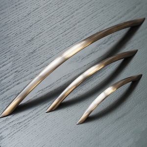 May include: Three silver-toned metal cabinet pulls in different sizes. The pulls are curved and have a brushed finish.