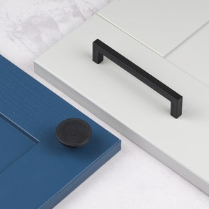 以下が含まれることがあります： 黒いキャビネット金具、ノブとプルが含まれています。ノブは丸型で、プルは長方形です。ノブは青いキャビネットドアに、プルは白いキャビネットドアに取り付けられています。