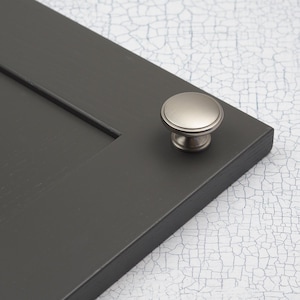 May include: A silver cabinet knob with a round, slightly raised top and a smooth, polished finish.