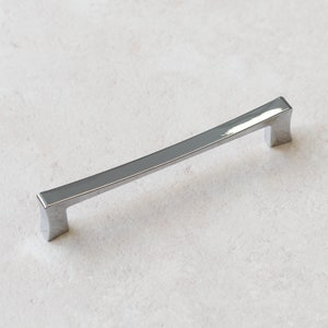 May include: A silver cabinet handle with a curved design.