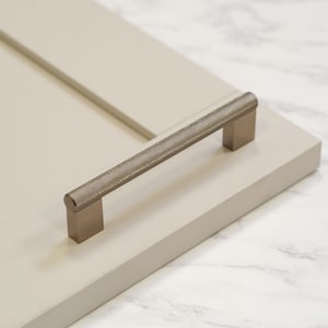 May include: A brushed nickel cabinet pull with a textured, diamond-shaped pattern. The pull is mounted on a white cabinet door.