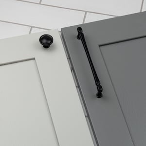 May include: Close-up of two cabinet doors, one white and one gray. The white door has a black round knob, while the gray door has a long, black handle. Both doors are set against a white tile background.