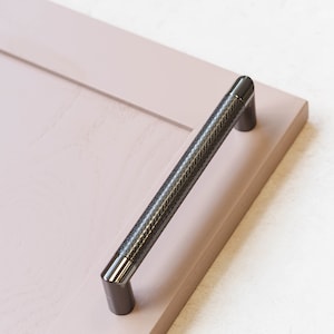 May include: A black cabinet pull with a textured diamond pattern. The pull is mounted on a light pink cabinet door.