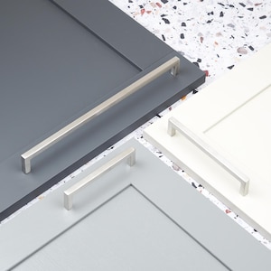 Puede incluir: Una colección de muestras de puertas de armario en gris, gris claro y blanco, cada una con un tirador de barra de níquel cepillado. Los tiradores varían en tamaño, con un tirador largo y varios más cortos. El fondo es un patrón de terrazo moteado.