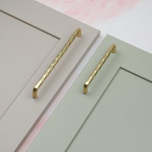 May include: Two gold cabinet pulls with a twisted design. The pulls are shown mounted on cabinet doors.