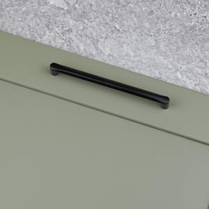 May include: Black cabinet pull with rounded ends. The pull is mounted on a light green cabinet door.