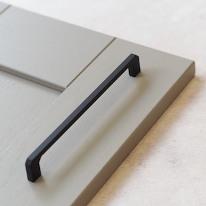 May include: Black cabinet door handle with a rectangular shape and a matte finish.
