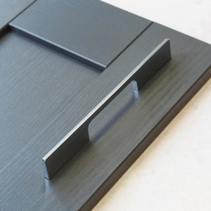 May include: A close-up of a silver cabinet door handle on a dark gray cabinet door.
