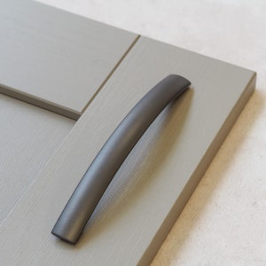 May include: A dark grey metal cabinet door handle with a curved design.