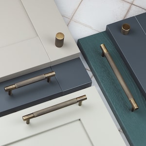 May include: A set of four cabinet hardware pieces in a brushed brass finish. The set includes two knobs and two pulls. The knobs are round and have a textured surface. The pulls are rectangular and have a textured surface. The hardware is shown on different colored cabinet doors.