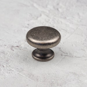 May include: A round, silver-toned cabinet knob with a slightly textured finish. The knob has a rounded base and a raised top.